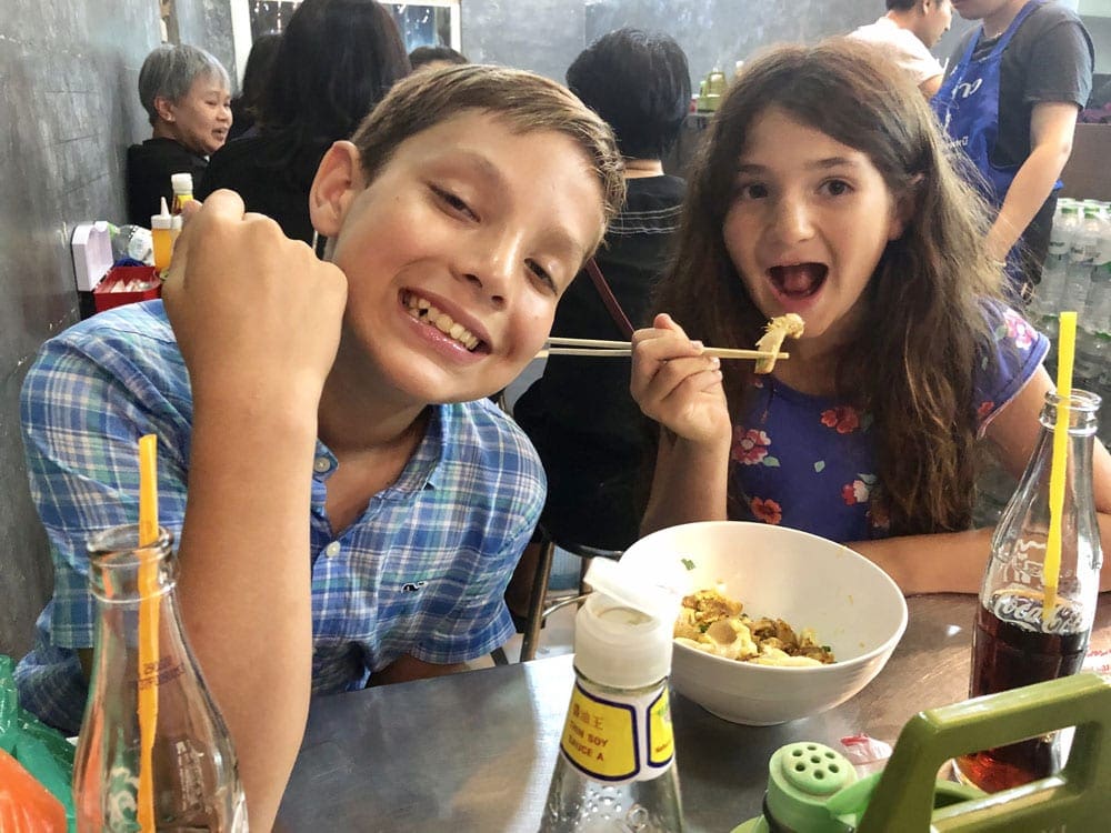 Two kids eating Thai food together, while visiting Bangkok, Thailand.