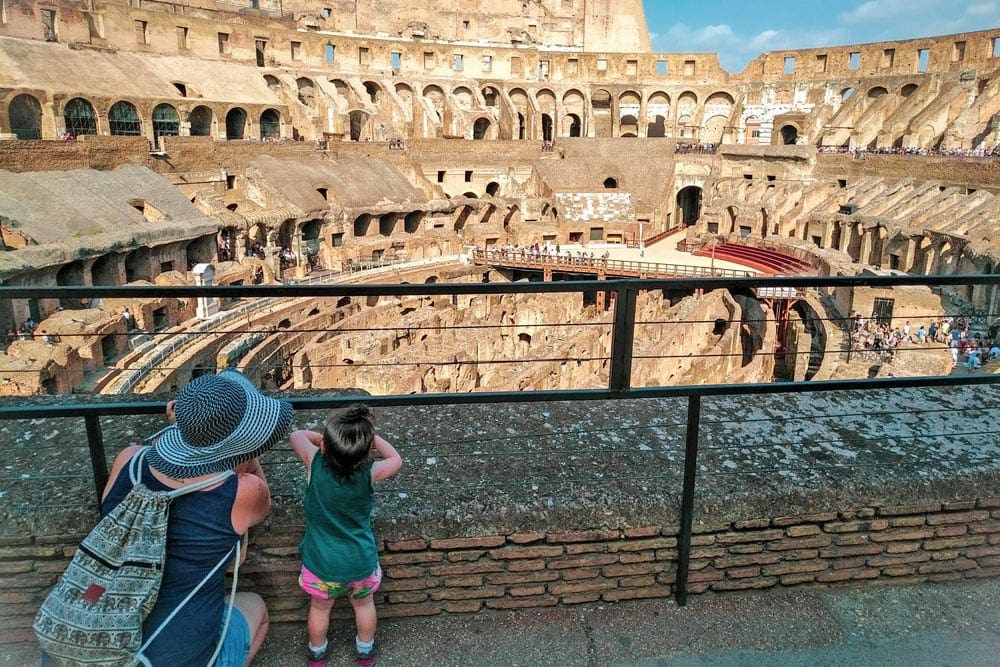 A mom and her young daughter look into the center of the Colosseum.