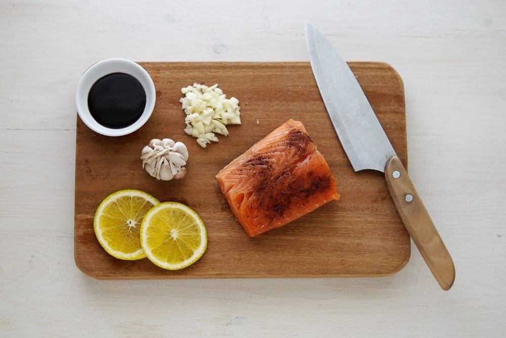 Dinner board with a knife, salmon, lemon, and garlic. Making a Norwegian-inspired recipe is a fantastic way to immerse yourself in a virtual vacation to Norway.