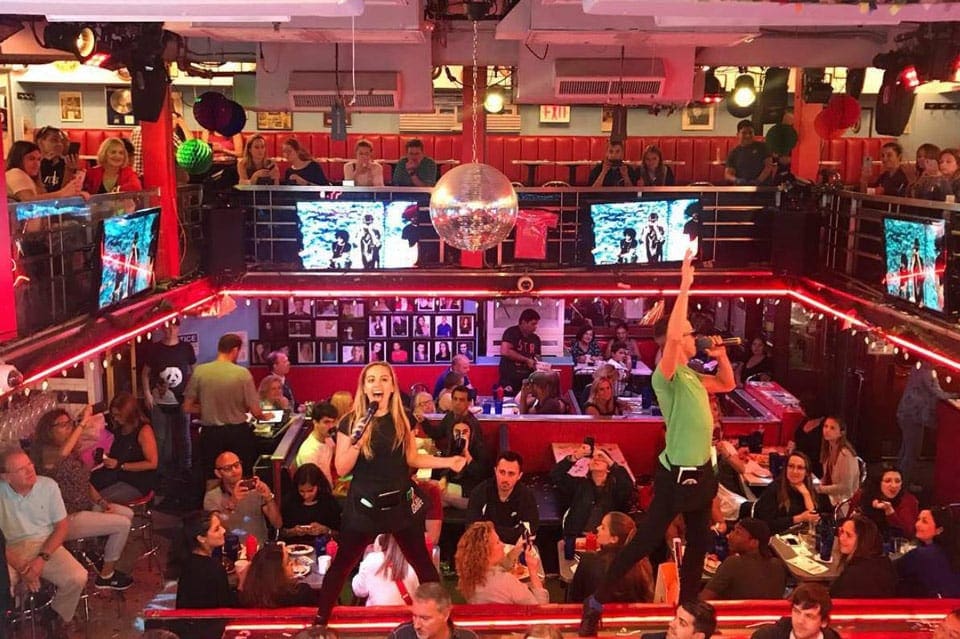 Two singers standing on tables put on a show to a room full of diners at Ellen’s Stardust Diner, one of the most unique New York City restaurants with Kids.