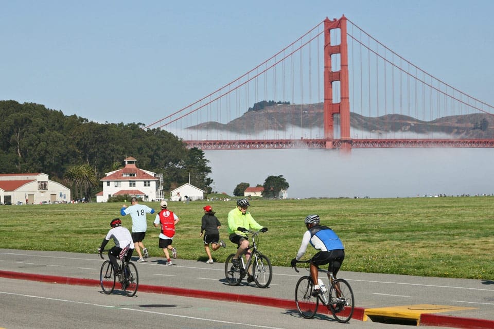 Several people bike along a path near the Golden Gate Bridge.