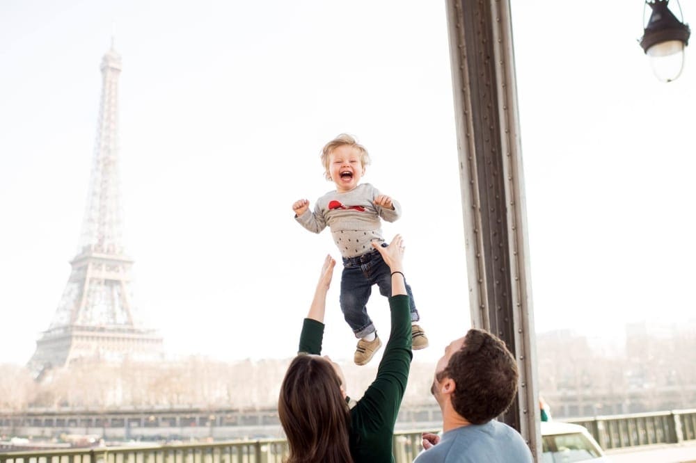 A parent throwing their kid into the air with the Eiffel Tower in the background in Paris, France.