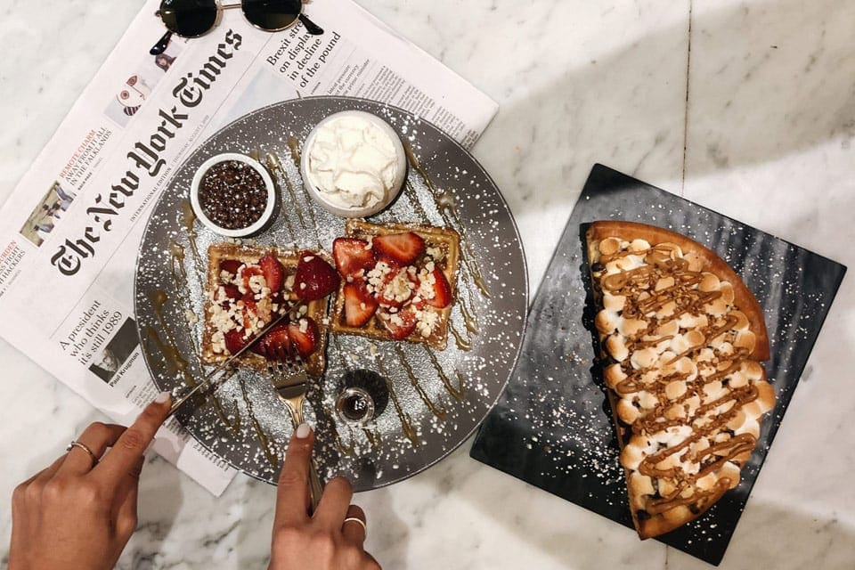 An overhead of someone cutting into their dinner, with a nearby piece of dessert at Max Brenner’s.