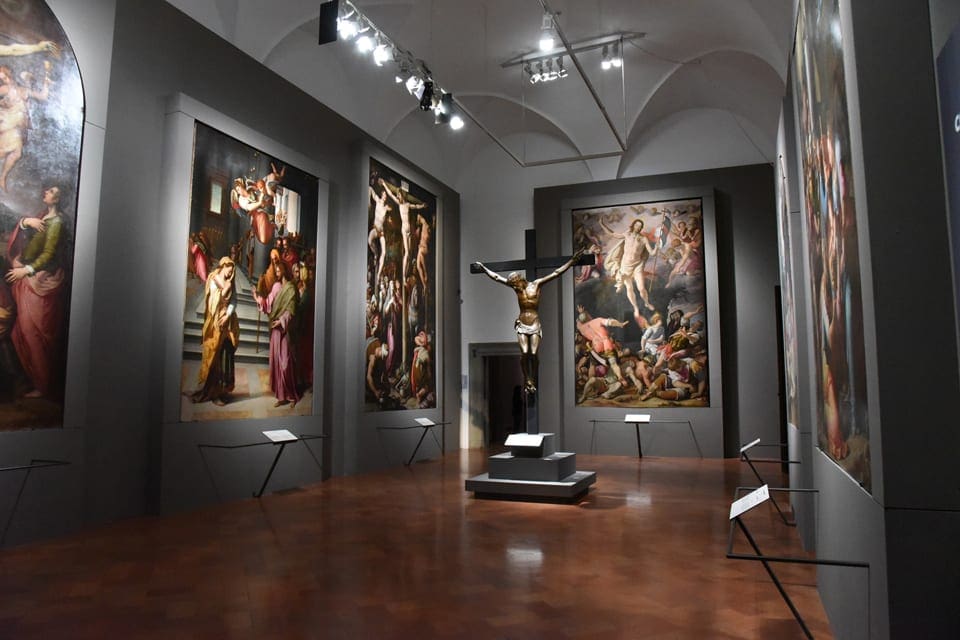 Inside one of the gallery rooms at the Palazzo Strozzi + Museum, featuring large paints and a crucifix statue in the center.