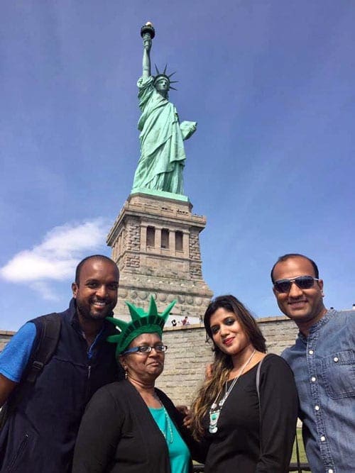 Four people stand togehter smiling with the Statue of Lib