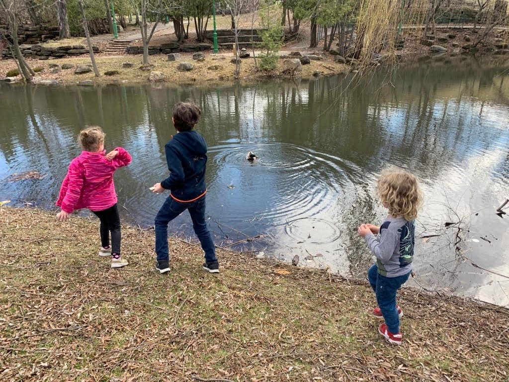 Three kids throw rocks into the water in Montreal.