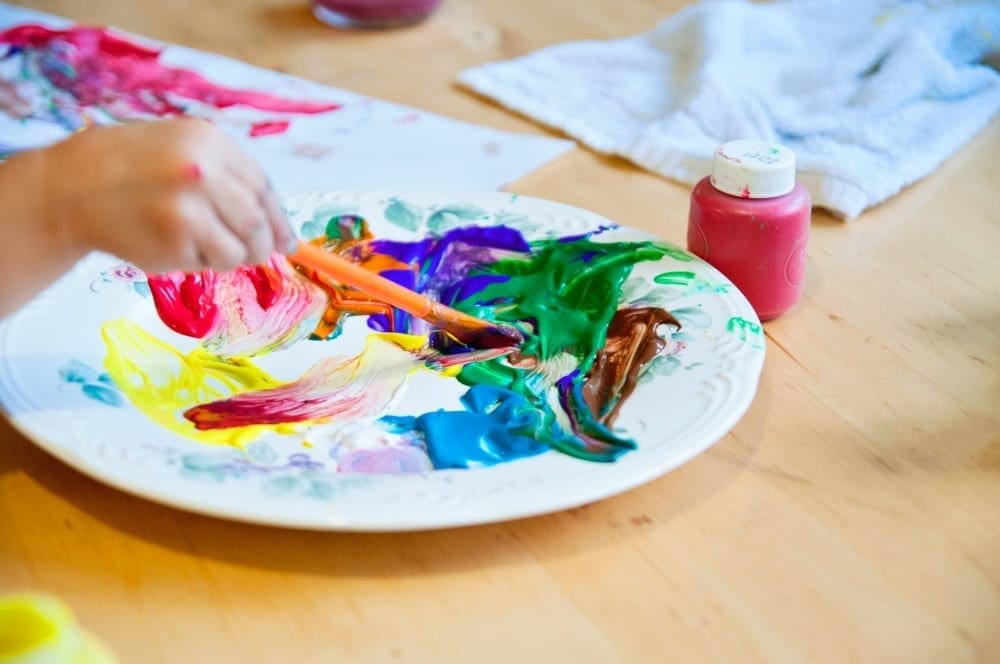 Art is one of the best ways to seek  is one of the best ways to seek Virtual Travel from Home to London. Childs hand is seen with paintbrush and many colors of paint.