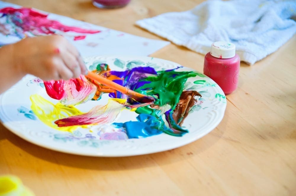 Art is one of the best ways to seek is one of the best ways to seek Virtual Travel from Home to London. Childs hand is seen with paintbrush and many colors of paint.