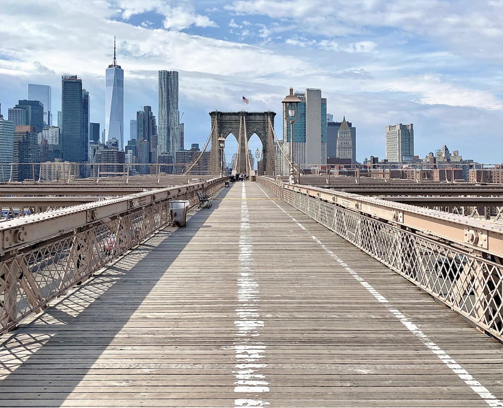 A view down the iconic Brooklyn Bridge on a sunny day, with the skyline of NYC in the distance. Brooklyn is one of the best places to visit on a Northeast road trip with kids. 