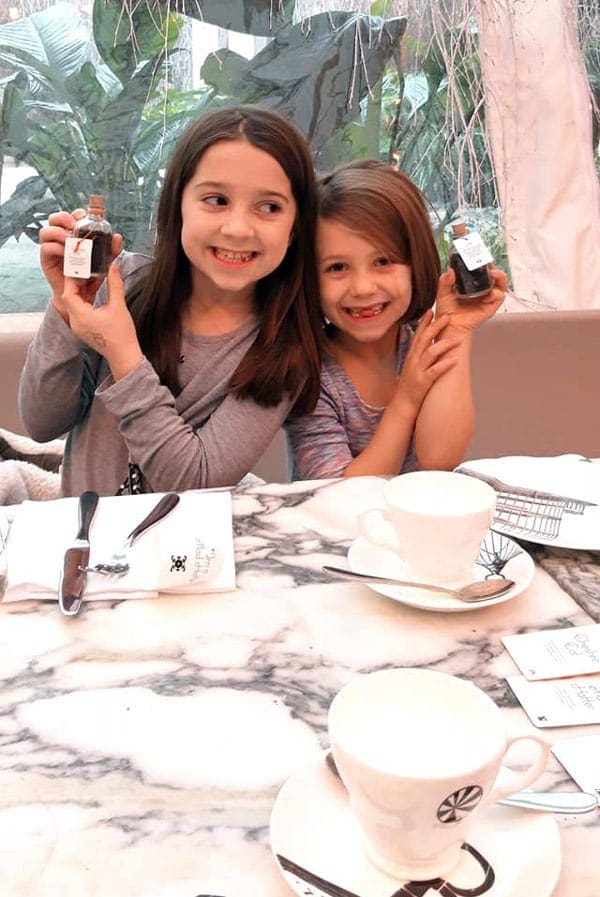 Two girls smile broadly, while enjoying tea time in London on a family trip.