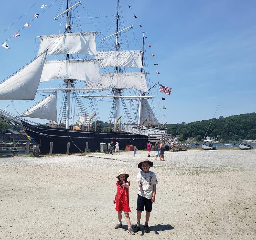 Boy and girl in front of a large ship in Mystic, Connecticut, one of the best places to visit during Memorial Day Weekend near NYC for families.