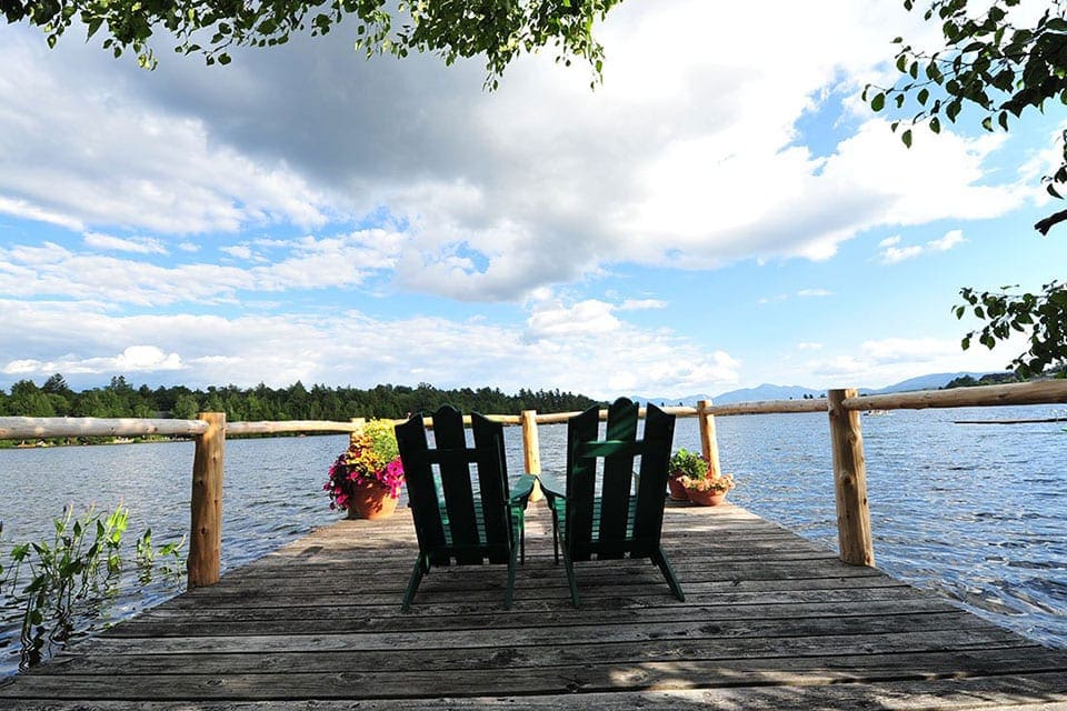 Two chairs sit on dock surrounded by flowers at Mirror Lake Inn, one of the best summer lake resorts in the Northeast for families.