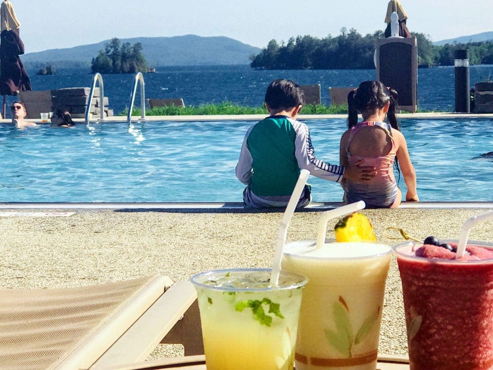 Boy and a girl facing the pool and the Lake George, one of the best lakes near New York City for families.