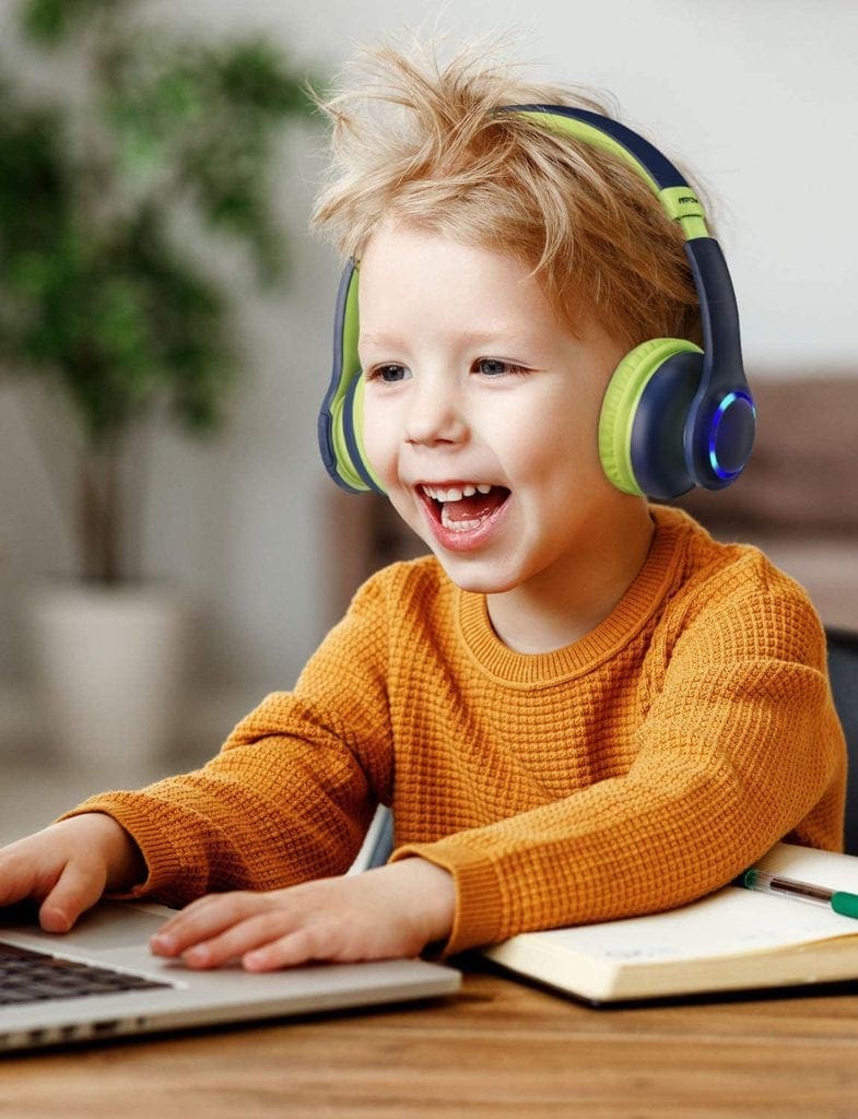 Little boy playing on the laptop wearing a pair of the best travel headphones for kids, the MPOW CH9 Kids Headphones.