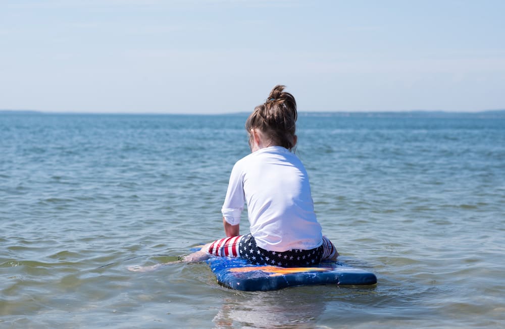 Little boy sitting on a surfboard in the water with exploring one of the best family beach trips near NYC.