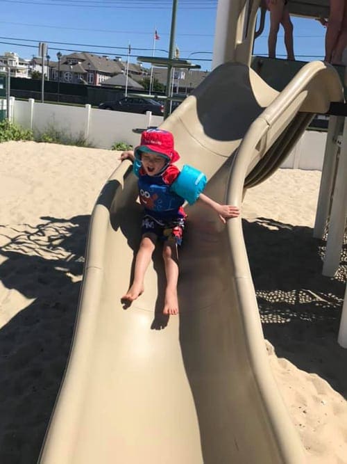 little boy in a puddle jumper coming down the slide in Long Island Beach