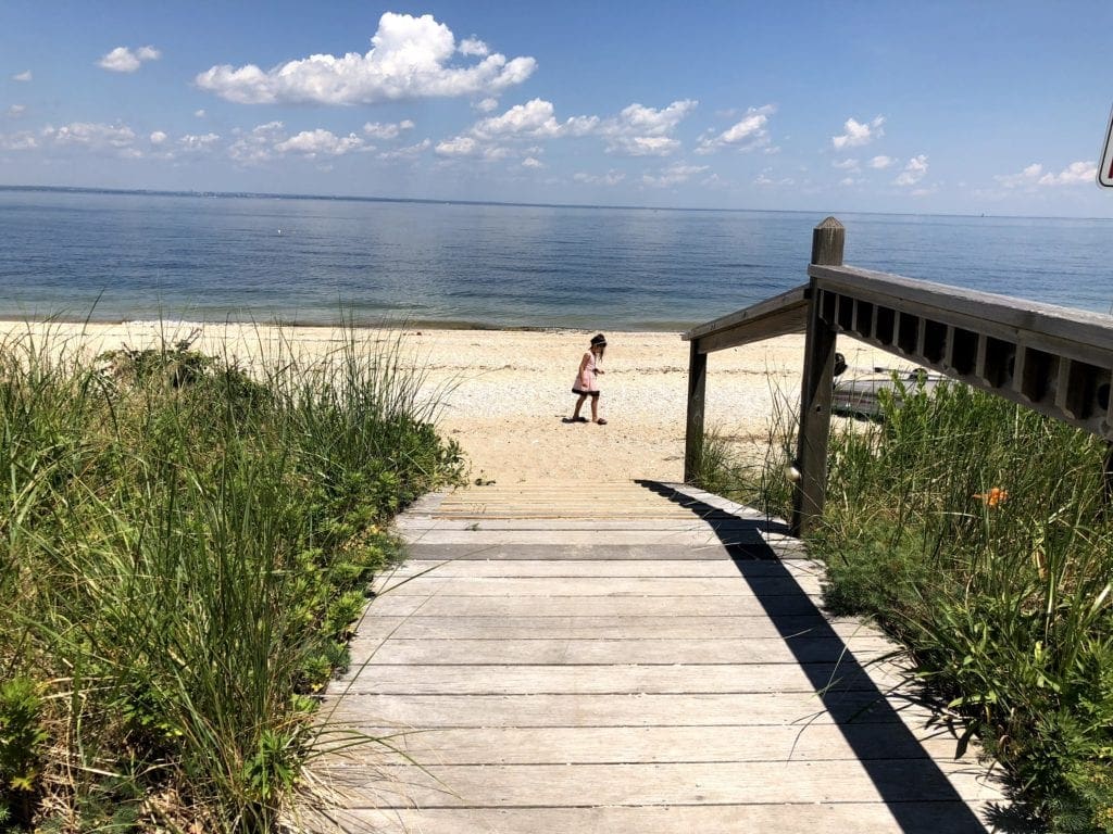 Little girl wearing a pink dress in the beach in Bayville, one of the best family beach trips near NYC.