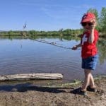 Young boy stands with a large stick in front of a lake.