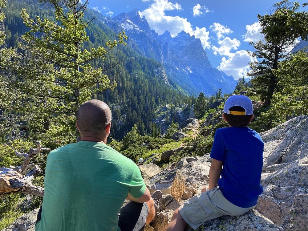 Father and son sit looking out onto the Grand Tetons.