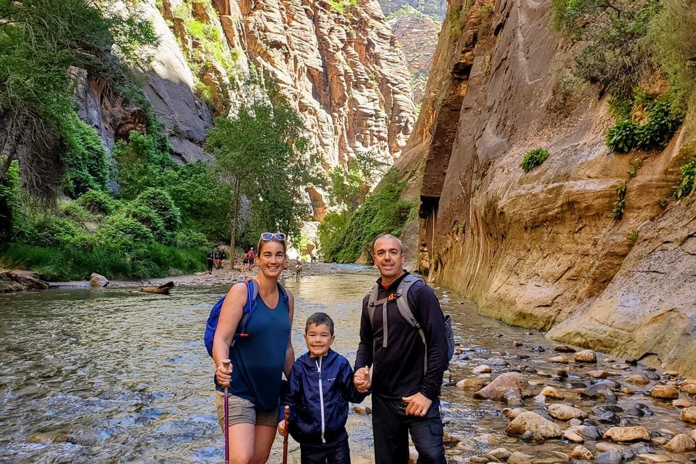 Family of three stands in a canyon at Zion National Park.