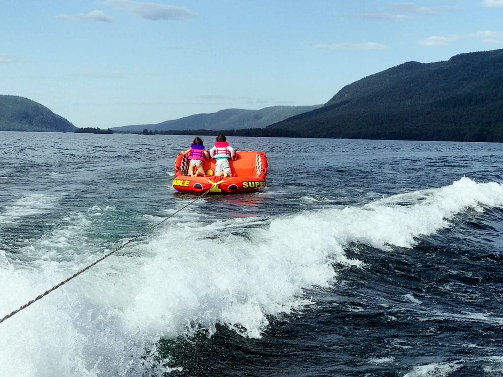 Boy and a girl in a orange towable tubing on Lake George.