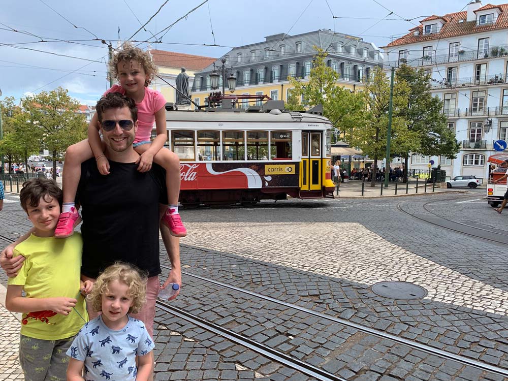 Father standing with two kids, and one kid on this shoulders, on a street in Lisbon, one of the best places to travel with kids in Europe.