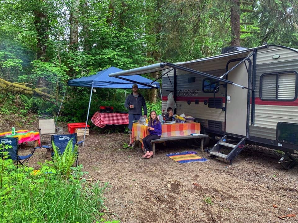 Family enjoying a meal at a camp site under a canopy of their RV