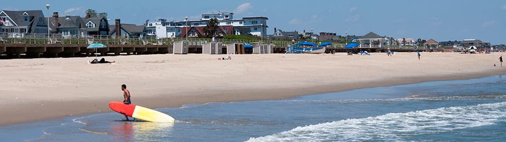 Man walking with surf board at Spring Lake, one of the best family beach trips near NYC.