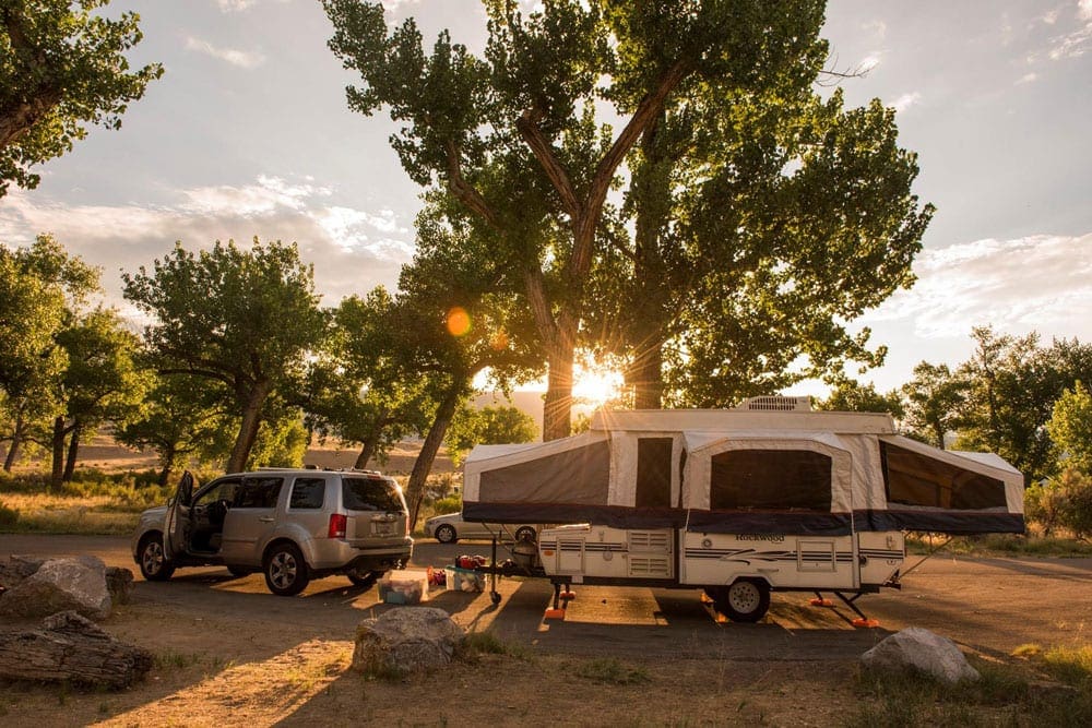 Pop-up RV trailed attached to SUV parked during sunset.