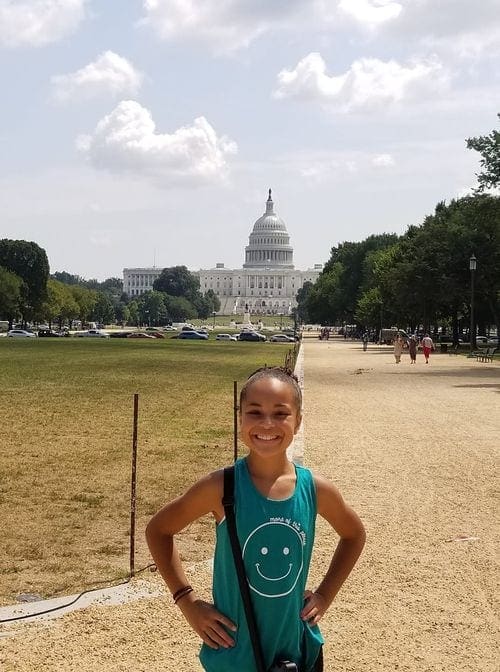 A young girl stands in front of the U.S. Capitol Building and lawn.