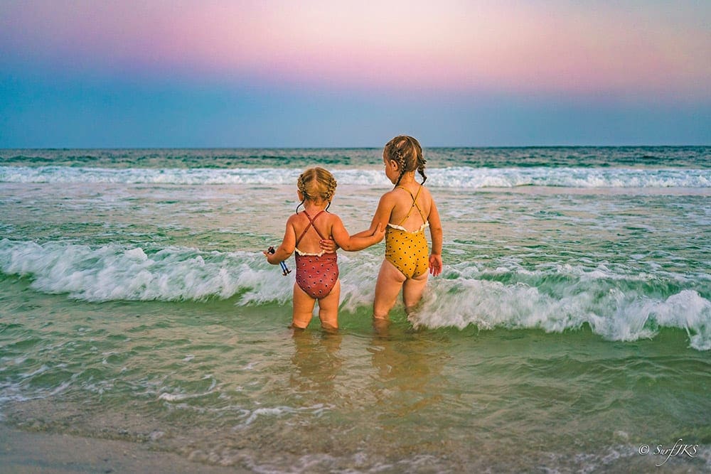 Two little girls with french braids standing in ocean off Pensacola Beach, one of the best Florida beaches for families.