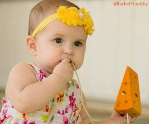 Baby girl with floral headband chewing on string of wooden cheese toy