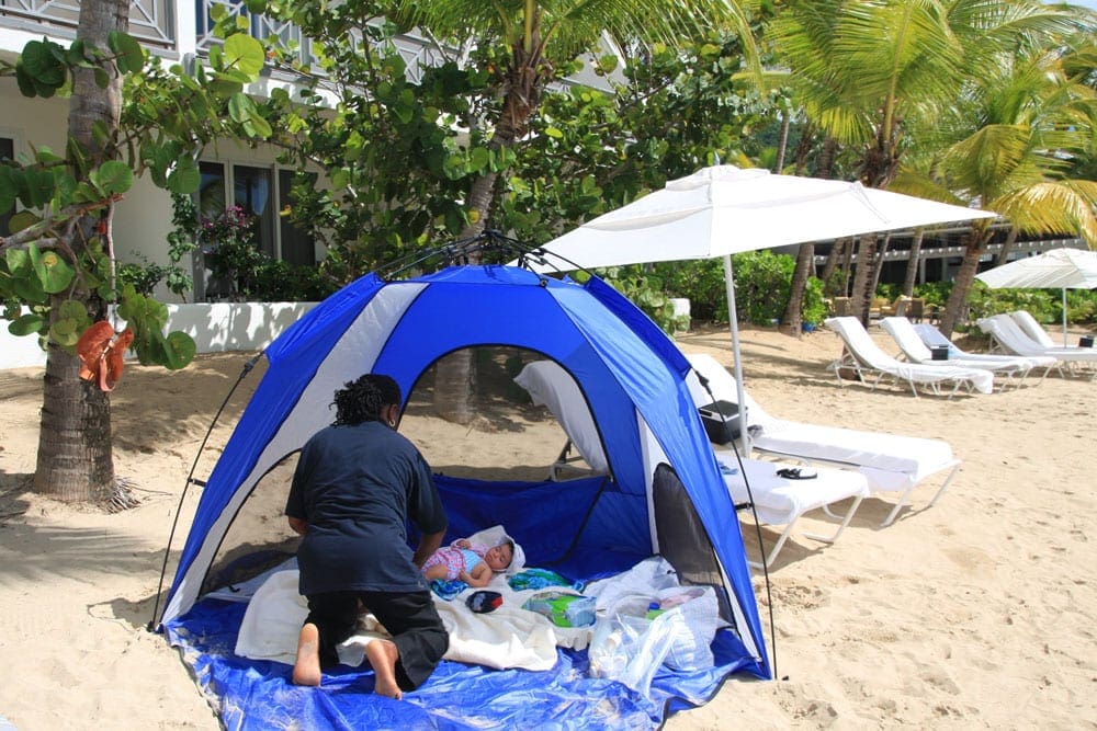 Baby in a tent with a babysitter on the beach at Carlisle Bay Hotel Find Babysitter Family Vacation