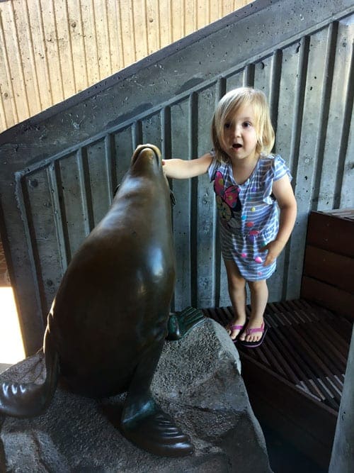Girl stands with a seal statue at the Seattle Aqarium.