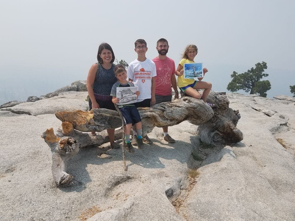 Family of five sits on a large wooden bench at Yosemite National Park.