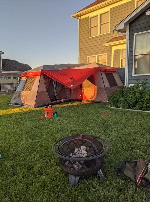 A red tent sits in the backyard prepared for camping at home.