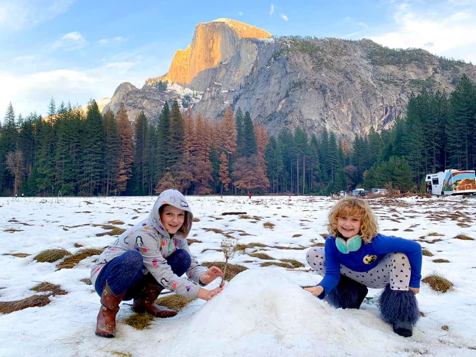 Two young girls sit and play in the snow at Yosemite National Park.
