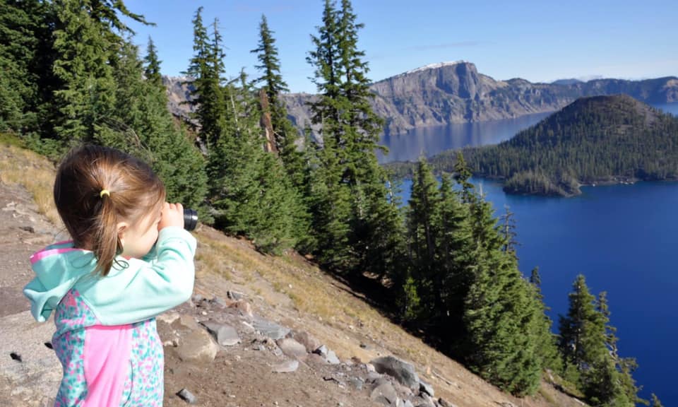 A young girl looks across the water through her binoculars.