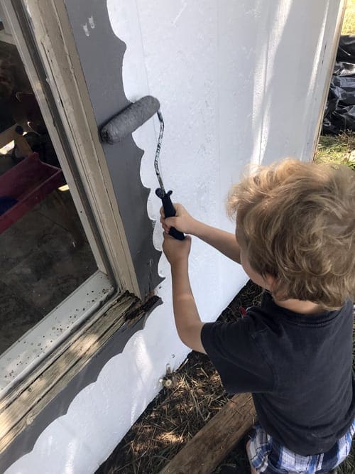 Small boy painting the trim of an outdoor window.