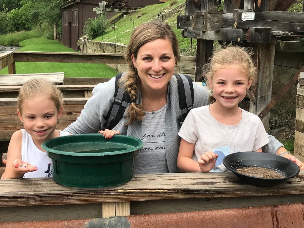 A mom and two young daughters sit smiling as they show off the gold they panned in South Dakota.