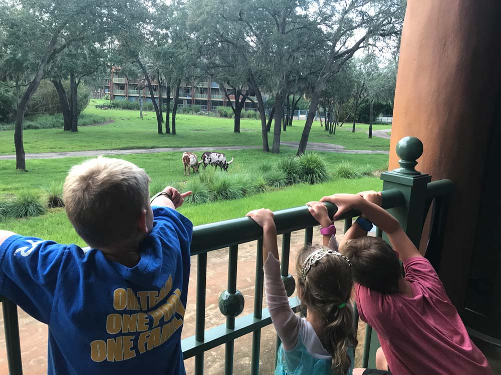 Three kids standing on balcony looking at animals at the Animal Kingdom Lodge in Disney World, a great Disney Deluxe Resort for families.