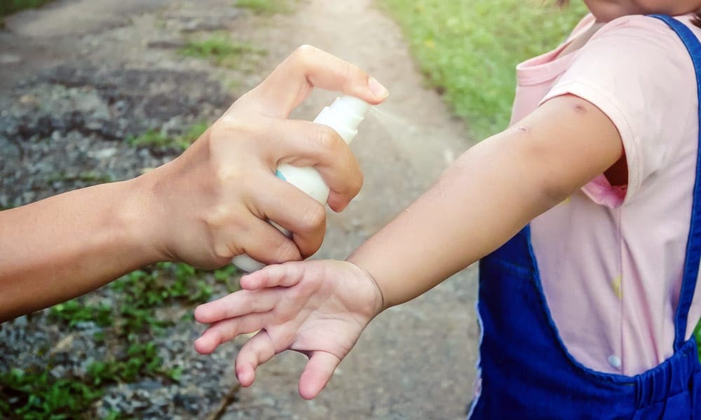 Hand with a bug spray bottle spaying the kids hand