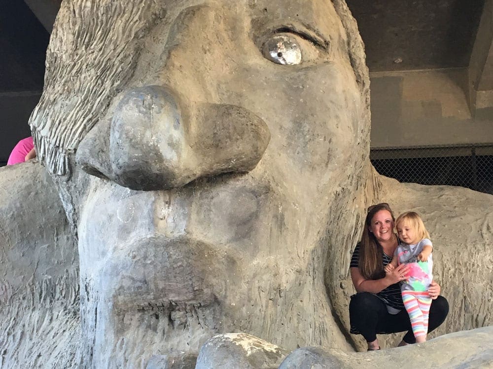 Mother and daughter stand on the arm of the Fremont Troll.