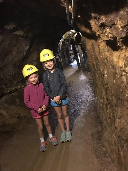 Two young girls wear yellow hardhats while on a mining tour inside a mining cave.