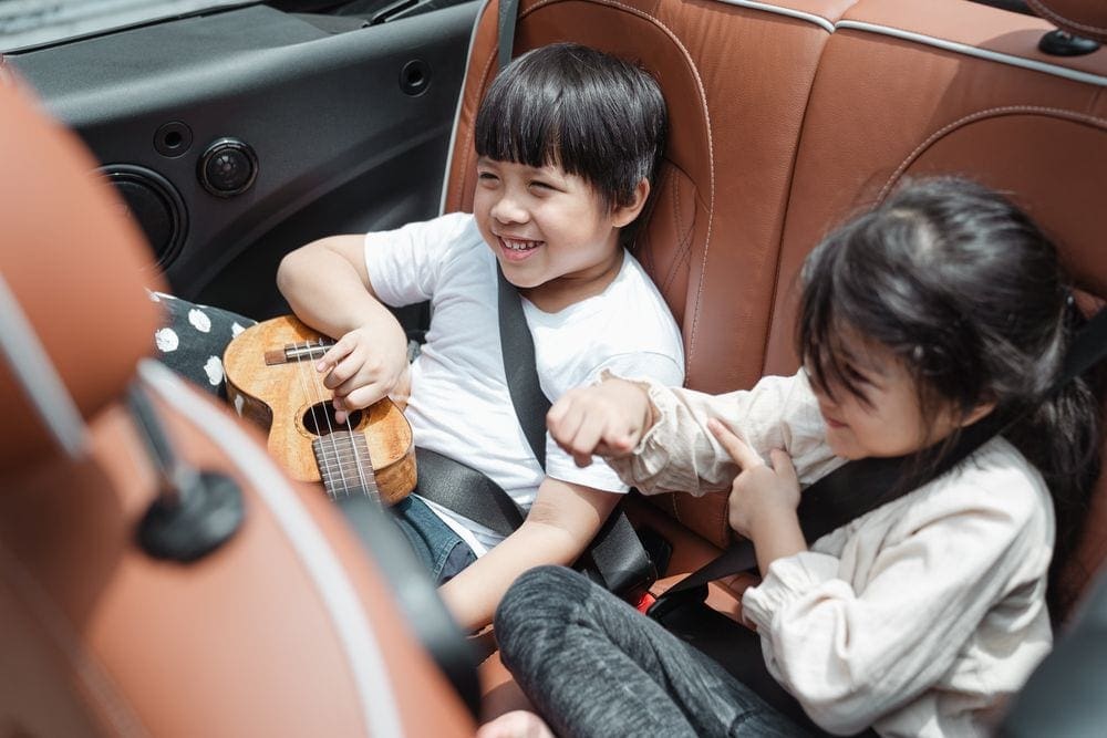 Two kids sit in the back seat, one holds a guitar.