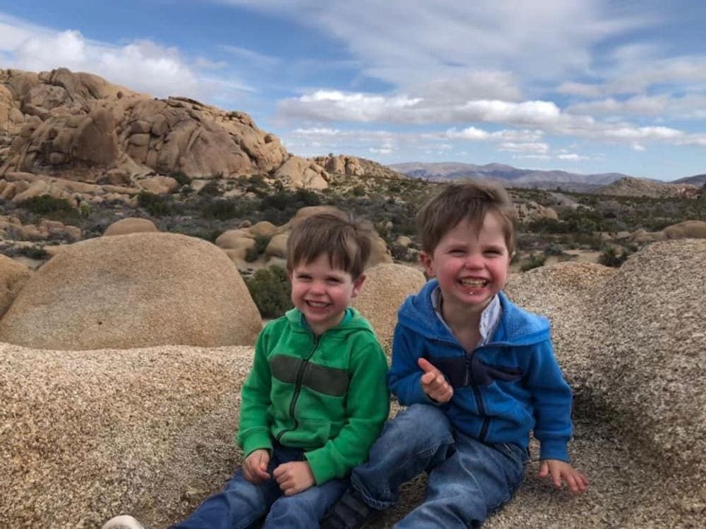 Two young boys sit laughing in Joshua Tree National Park, one of the best places to visit in California with kids. 