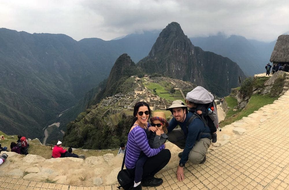 A family of four stands in front of an expansive view of Machu Picchu in the backgrund.