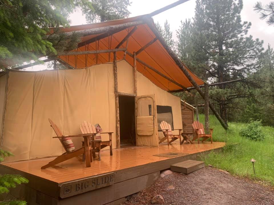 A view of the front of a large luxury tent with four adirondack chairs perched on the deck.