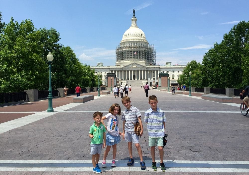Four kids stand smiling in front of the United States capitol building in Washington DC.
