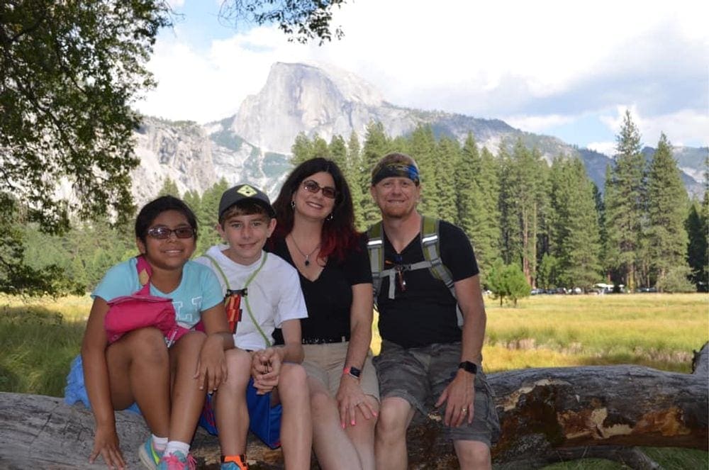 A family of four sits upon a log in front of a mountain view at Yosemite National Park.